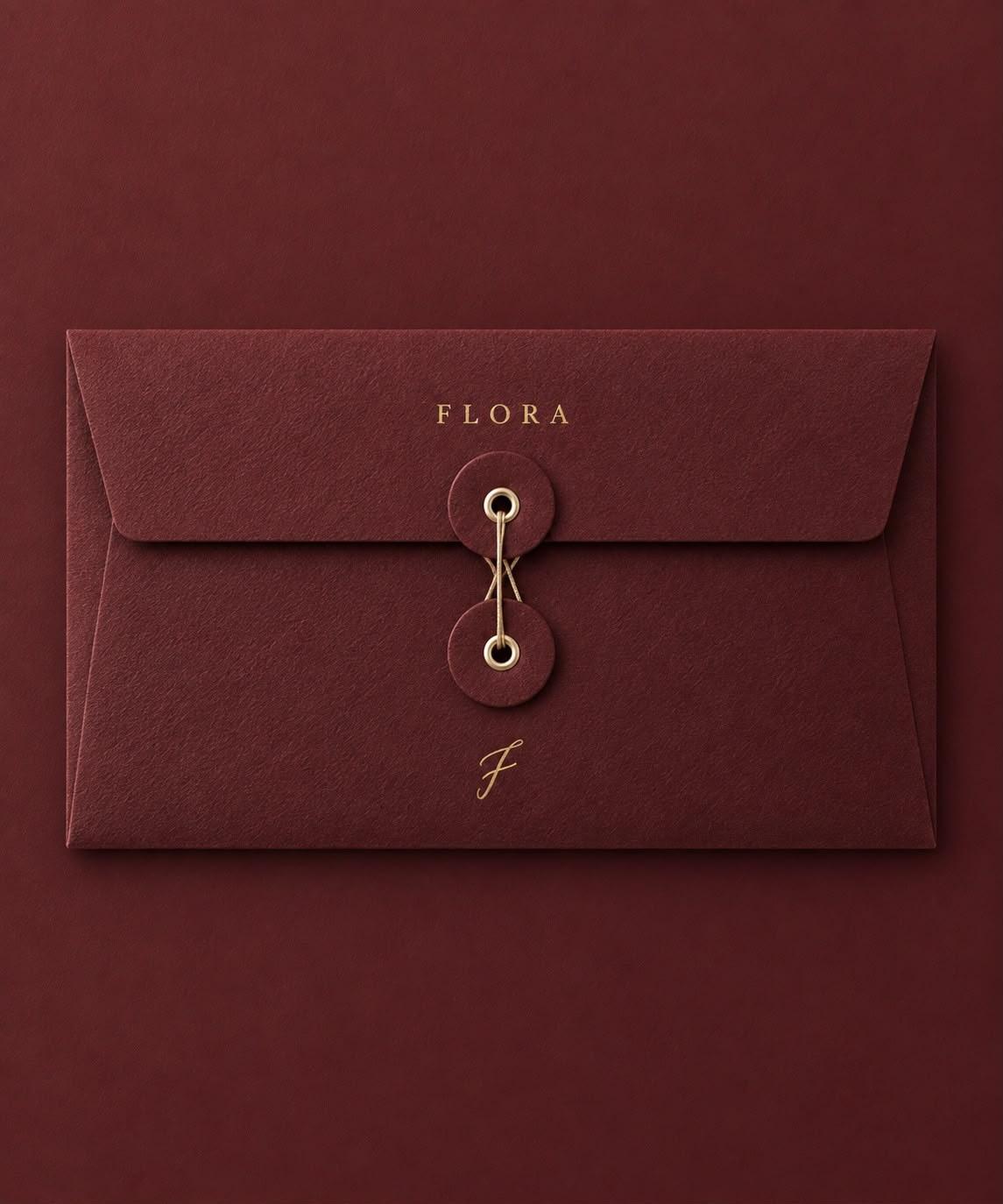 Oxblood FLORA envelope with a gold string-tie closure and script F monogram