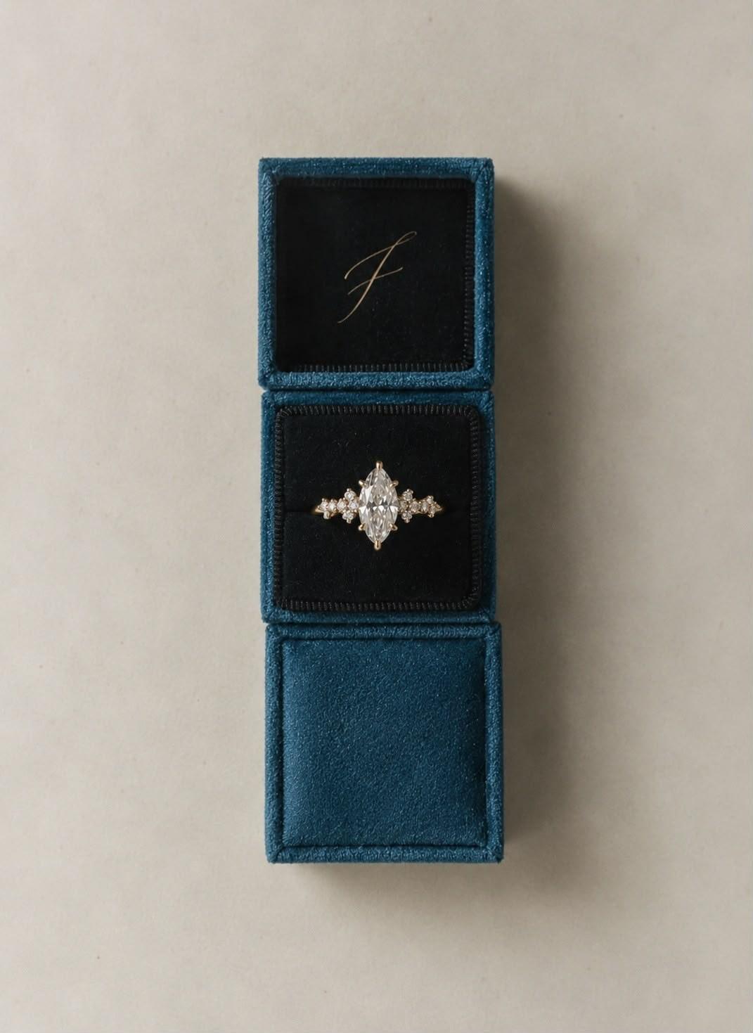 ANDËRR Ring in the middle of three stacked petrol velvet FLORA boxes, the top one embossed with a script F
