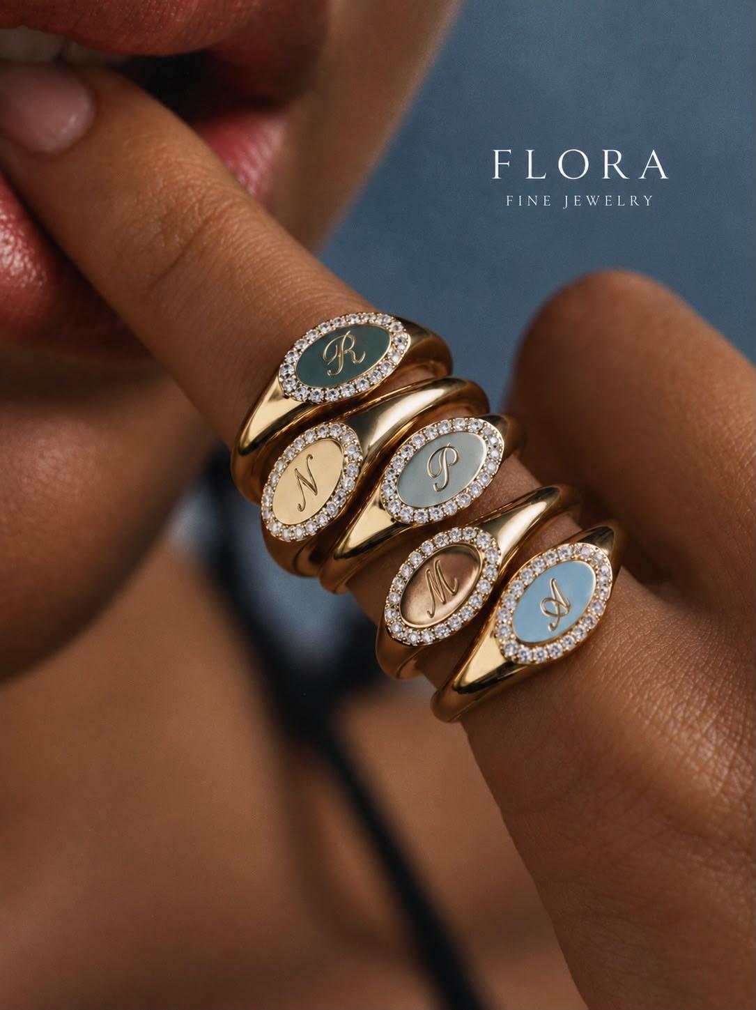 Five oval initial signet rings with diamond halos and coloured faces, worn across the fingers of a hand