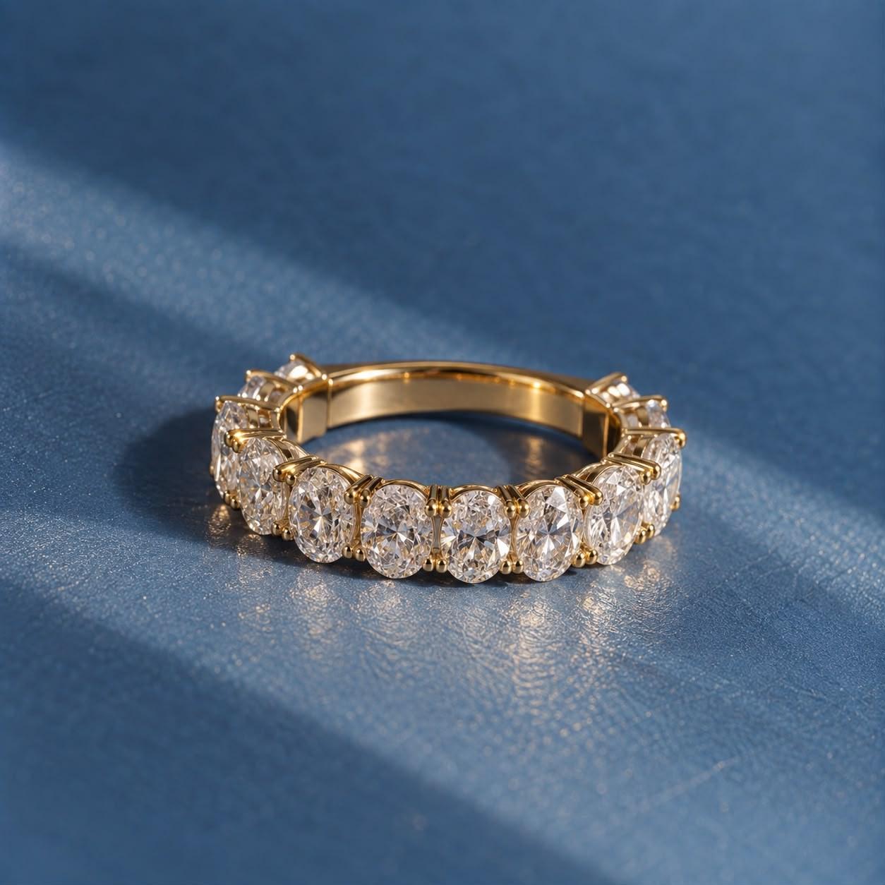 Oval diamond eternity band in 14K yellow gold on blue linen in a band of sunlight