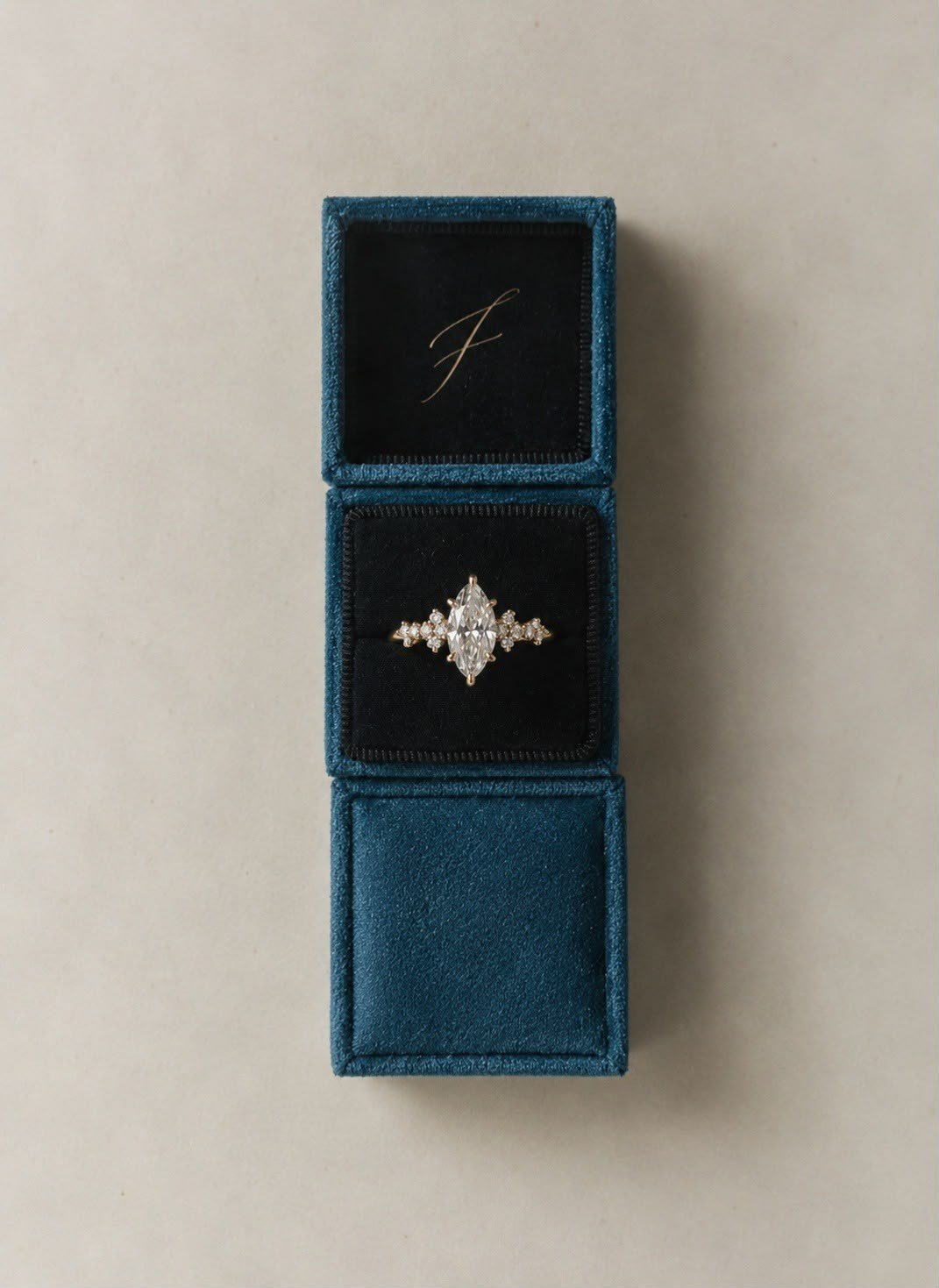 ANDËRR Ring in the middle of three stacked petrol velvet FLORA boxes, the top one embossed with a script F