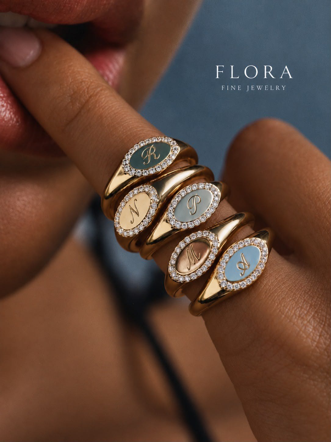 Five oval initial signet rings with diamond halos and coloured faces, worn across the fingers of a hand