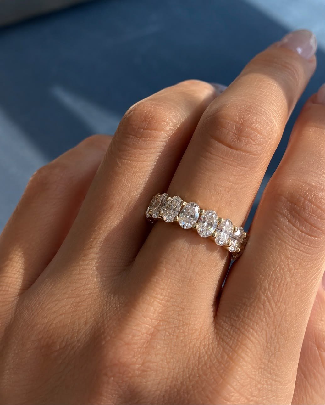 Oval diamond eternity band worn on a hand in sunlight