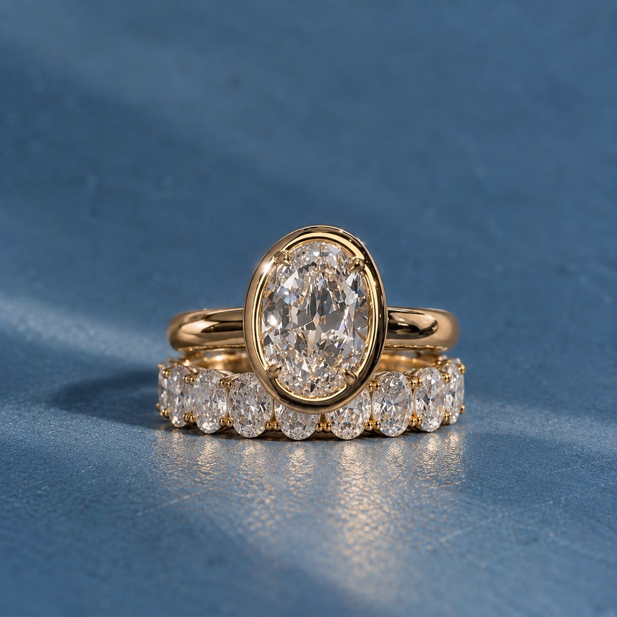Oval bezel ring stacked on an oval diamond eternity band on blue fabric