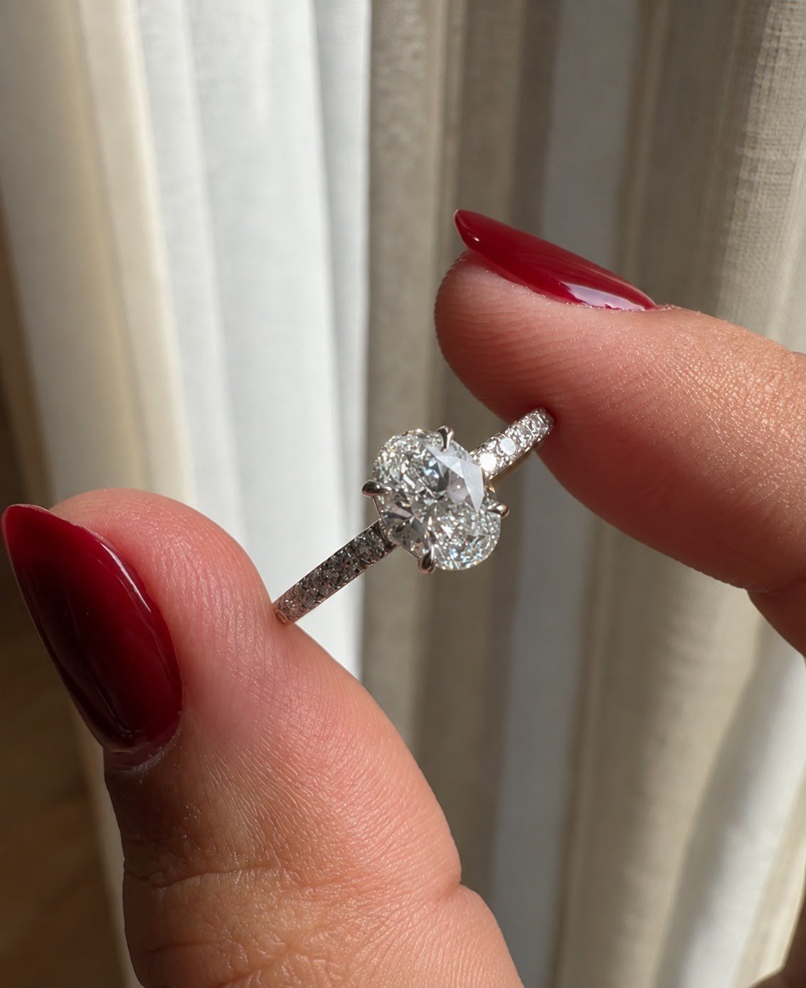 Oval pavé ring held between fingertips against a linen curtain
