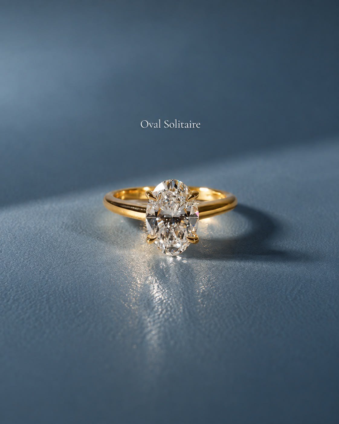 The Oval Solitaire in yellow gold standing on steel-blue leather