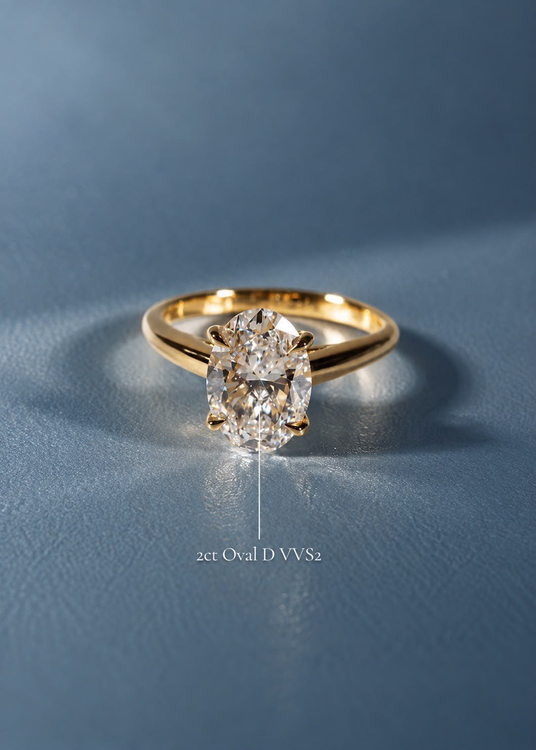 Yellow gold 2ct oval solitaire on slate-blue leather, with the stone's grade noted beside it