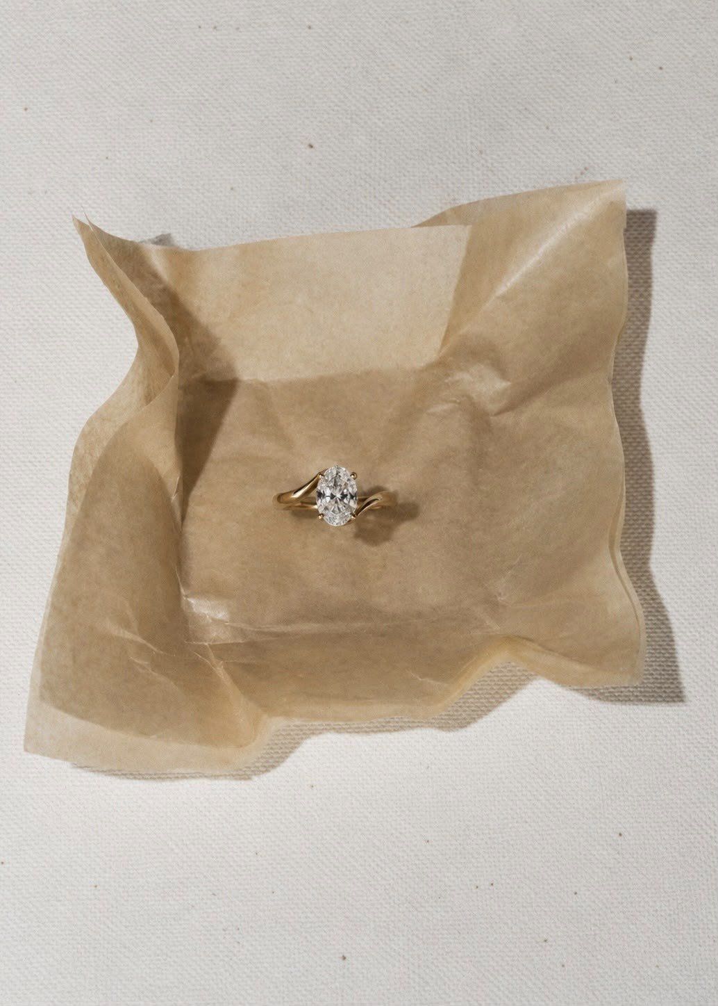 The Oval bypass solitaire resting on crumpled kraft tissue over linen