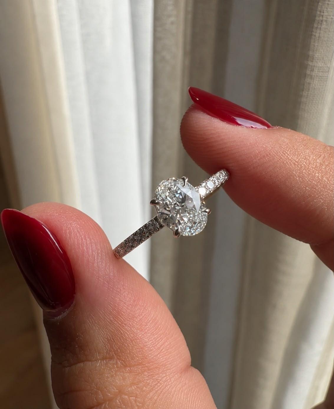 Oval pavé ring held between fingertips against a linen curtain