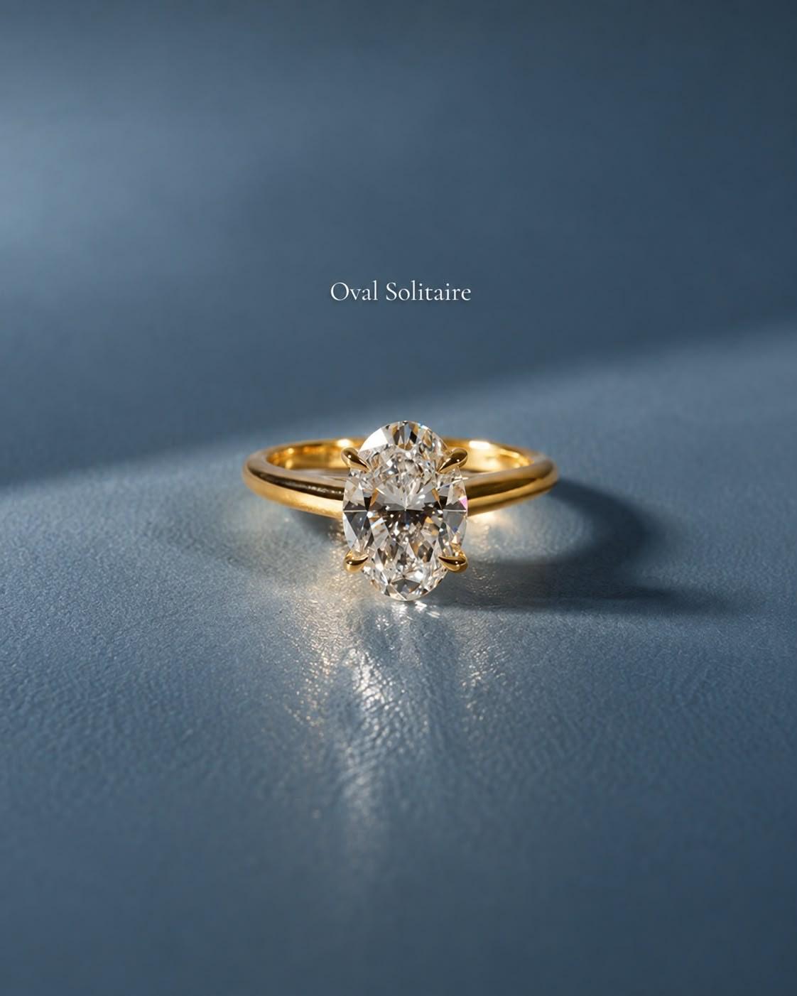The Oval Solitaire in yellow gold standing on steel-blue leather